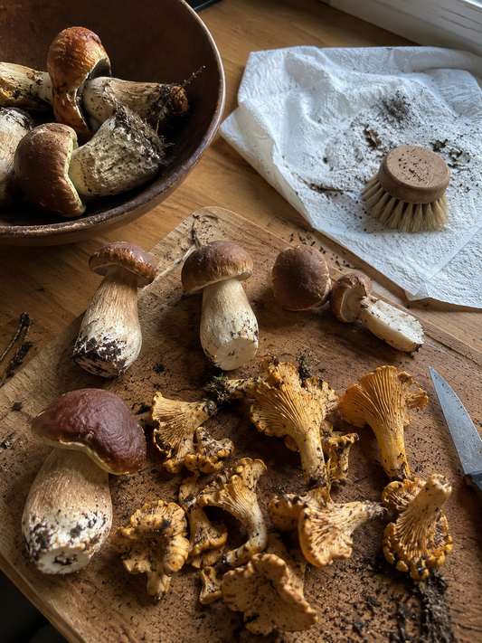 Nettoyage de cèpes et girolles fraîchement récoltés sur une planche en bois avant préparation en cuisine.